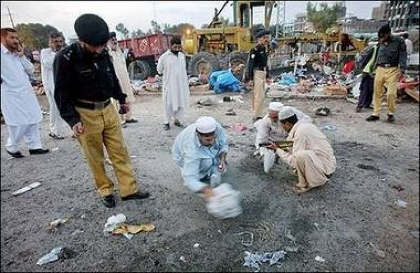 پشاور، پولیس اہلکار بم دھماکے کی جگہ سے بم کے ٹکڑے اٹھا رہے ..