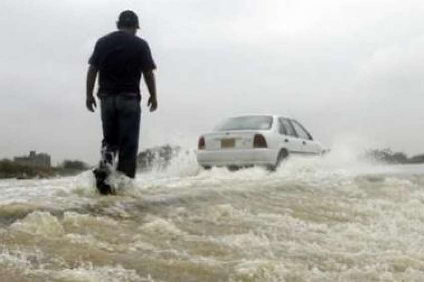 کراچی،ایک شخص بارش کے پانی میں‌بھری سڑک پار کر رہا ہے۔