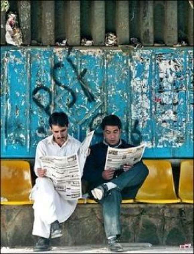 اسلام آباد، بس سٹاپ پر بیٹھے دو نوجوان اخبارات کا مطالعہ ..