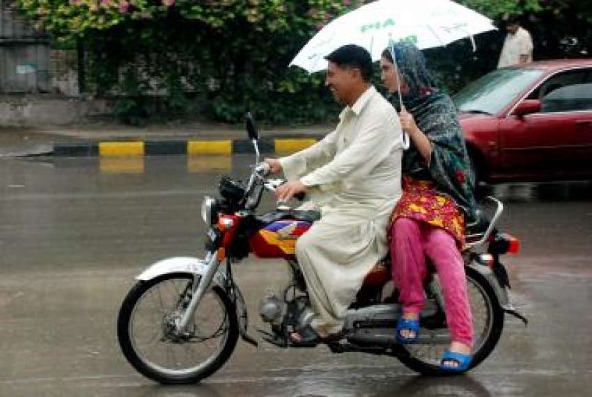لاہور، دو موٹر سائیکل سوار بارش سے بچنے کیلئے چھتری تانے ..