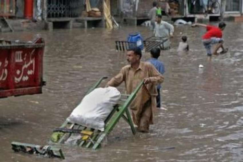 لاہور،ایک شخص بارش کے بعد کھڑے ہونیوالے پانی میں اپنی ریڑھی ..