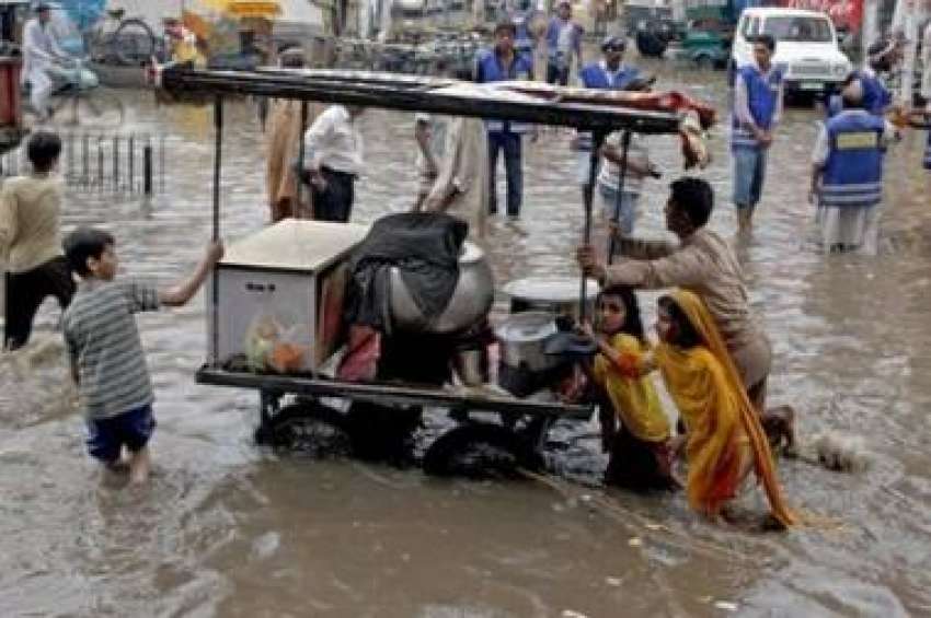 لاہور،ایک شخص اپنے بچوں‌کے ہمراہ بارش کے بعد کھڑے پانی ..