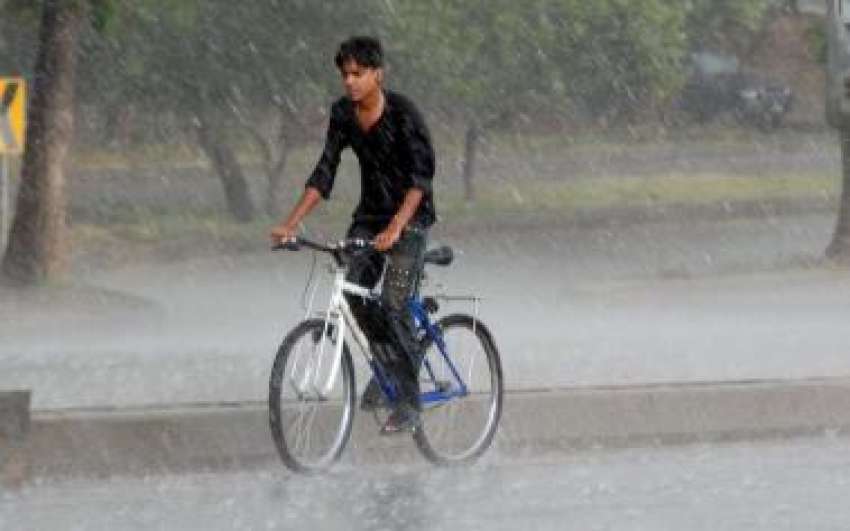 اسلام آباد، شدید گرمی کے بعد بارش میں ایک نوجوان سائیکل ..