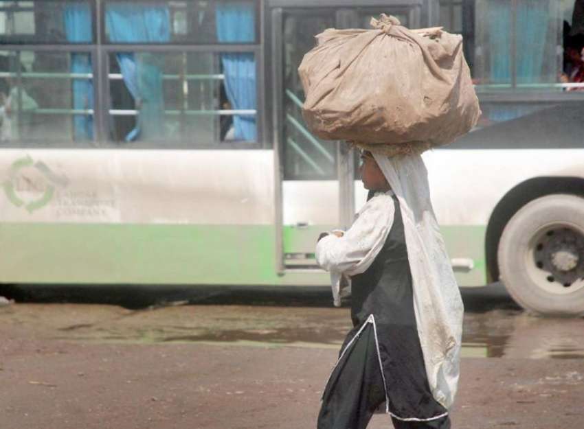 لاہور: ایک مسافر خاتون سر پر سامان اٹھائے بس میں سوار ہونے ..