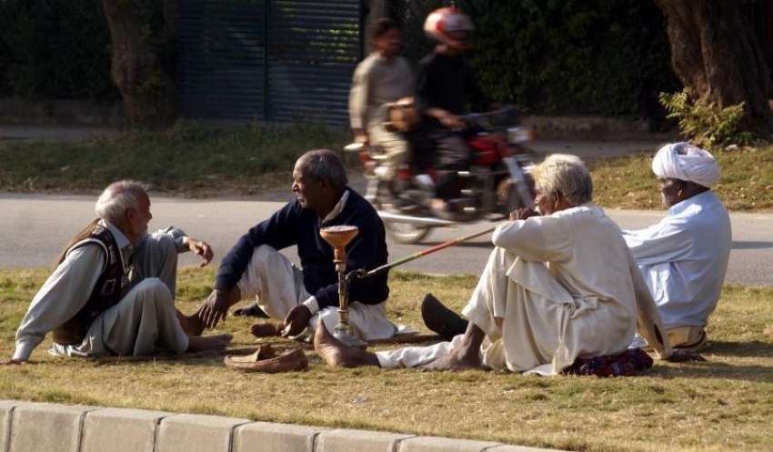اسلام آباد، معمر افراد کا ایک گروپ سڑک کنارے بیٹھے دھوپ ..
