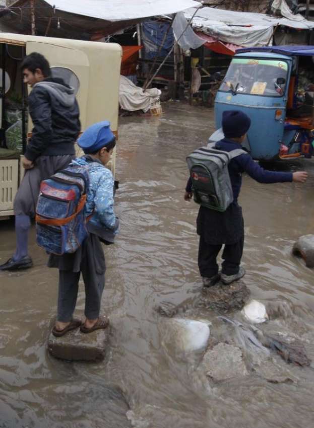 پشاور، سکول کے بچے بارش کے پانی سے بچنے کیلئے پتھروں پر چل ..