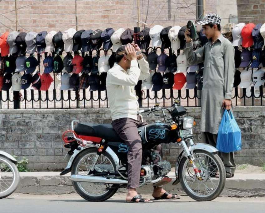 لاہور: ایک موٹر سائیکل سوار شخص دھوپ سے بچنے کے لیے سڑک کنارے ..