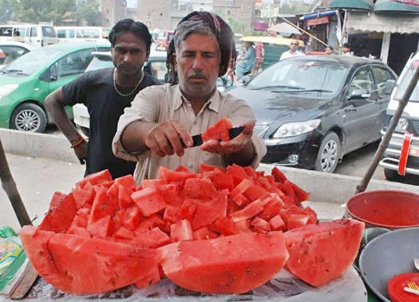 لاہور: ایک محنت کش ریڑھی پر تربوز فروخت کرنے کے لیے کاٹ رہا ..