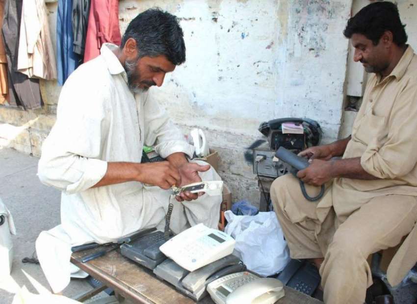 لاہور: دو کاریگر سڑک کنارے فٹ پاتھ پر بیٹھے ٹیلی فون مرمت ..