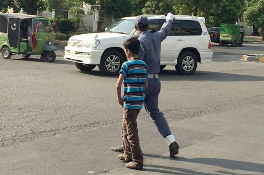 لاہور: گلبرگ کے قریب ایک ٹریفک وارڈن بچے کو سڑک عبور کروا ..