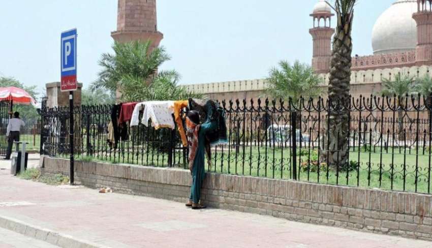 لاہور: بادشاہی مسجد کے جنگلوں پر ایک خاتون کپڑے خشک کرنے ..
