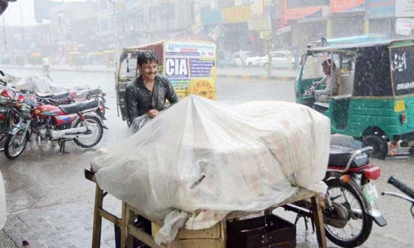 فیصل آباد: ایک دکاندار تیز بارش کے باعث اپنی دکان کے باہر ..