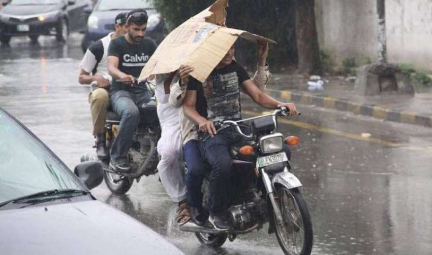 لاہور: موٹر سائیکل سوار بارش سے بچنے کے لیے سر پر گتہ رکھے ..