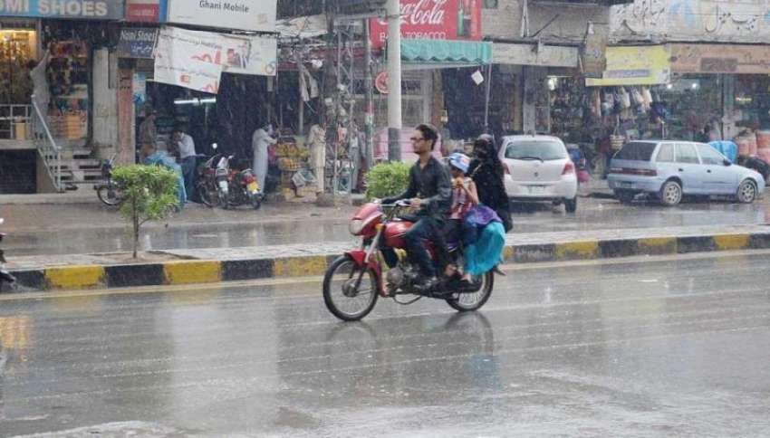فیصل آباد: بارش کے دوران ایک موٹر سائیکل سوار اپنی منزل کی ..