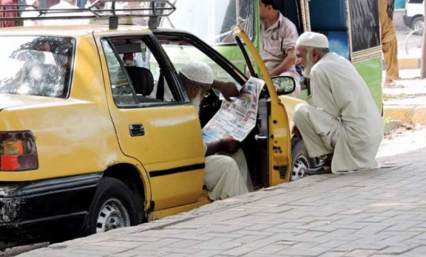 لاہور: مال روڈ پر ٹیکسی ڈرائیور فرصت کے لمحات میں اخبار پڑھ ..
