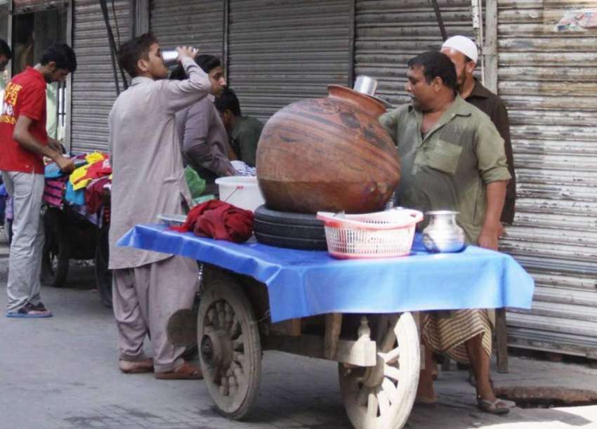 لاہور: ایک شخص گرمی کی شدت کم کرنے کے لیے ریڑھی والے سے لسی ..