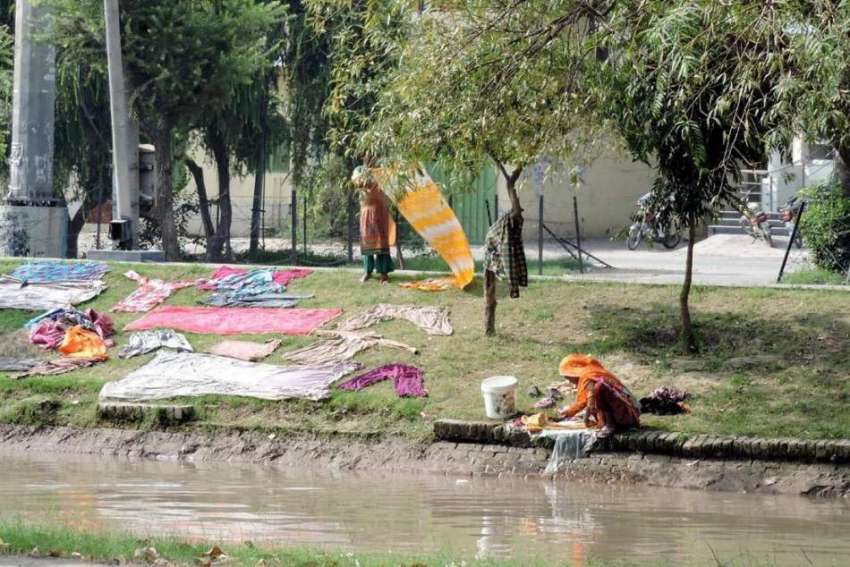 لاہور: ایک خانہ بدوش خاتون نہر کنارے بیٹھی کپڑے دھو رہی ہے۔