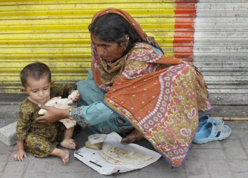لاہور: ایک بھکاری خاتون سڑک کنارے فٹ پاتھ پر بیٹھی اپنے بچے ..