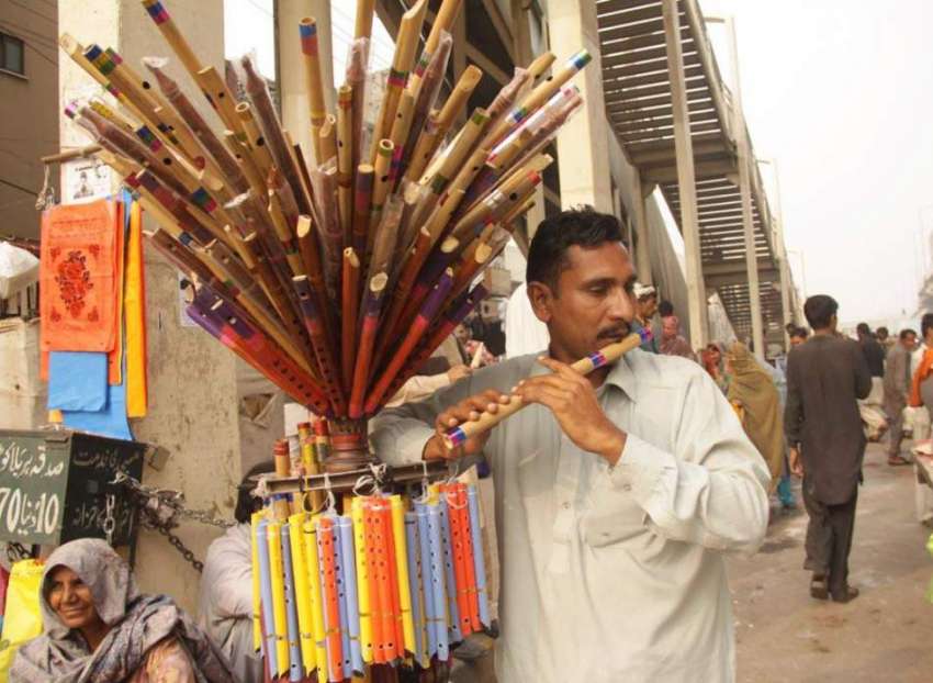 لاہور: ایک محنت کش گاہکوں کو متوجہ کرنے کے لیے بانسری بجا ..