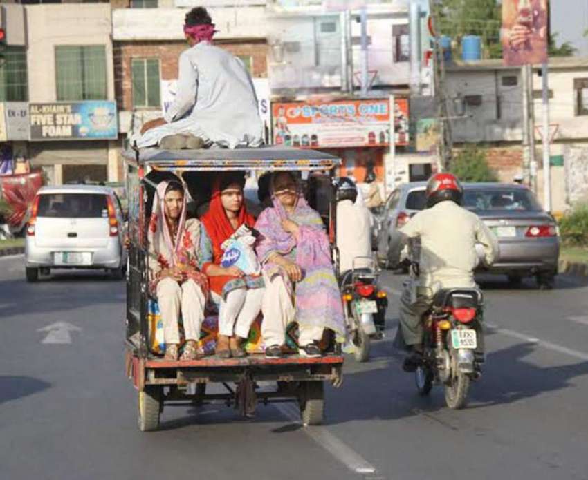 لاہور: ایک شخص موٹر سائیکل رکشے کی چھت پر بیٹھ کر سفر کر رہا ..
