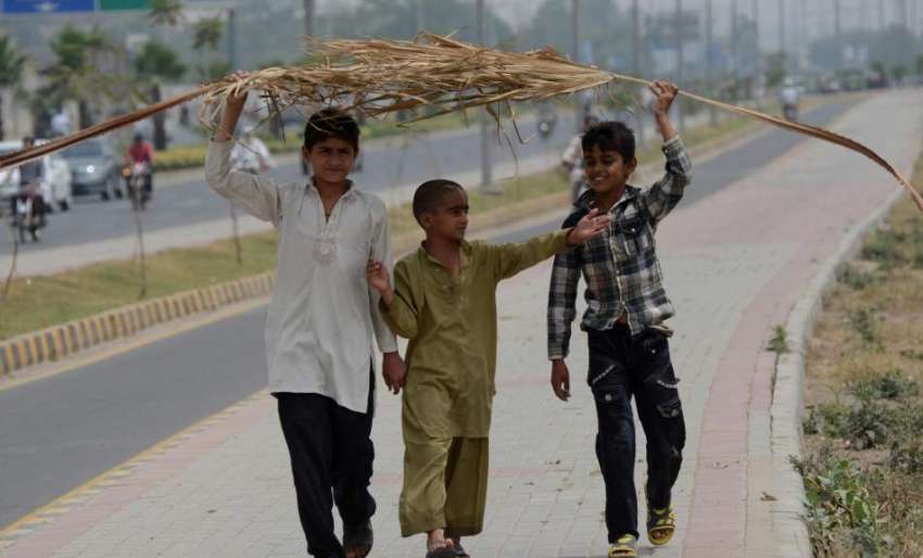 لاہور: دھوپ کی شدت سے بچنے کے لیے بچے کھجور کے پتوں کی چھتری ..