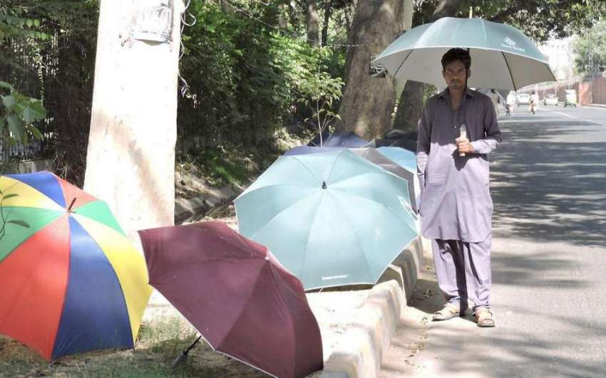 لاہور: چھتریاں فروخت کرنے کے لیے سڑک کنارے کھڑے ایک محنت ..