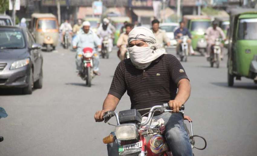 لاہور: ایک موٹر سائیکل سوار شہری دوپہر کے وقت شدید دھوپ سے ..
