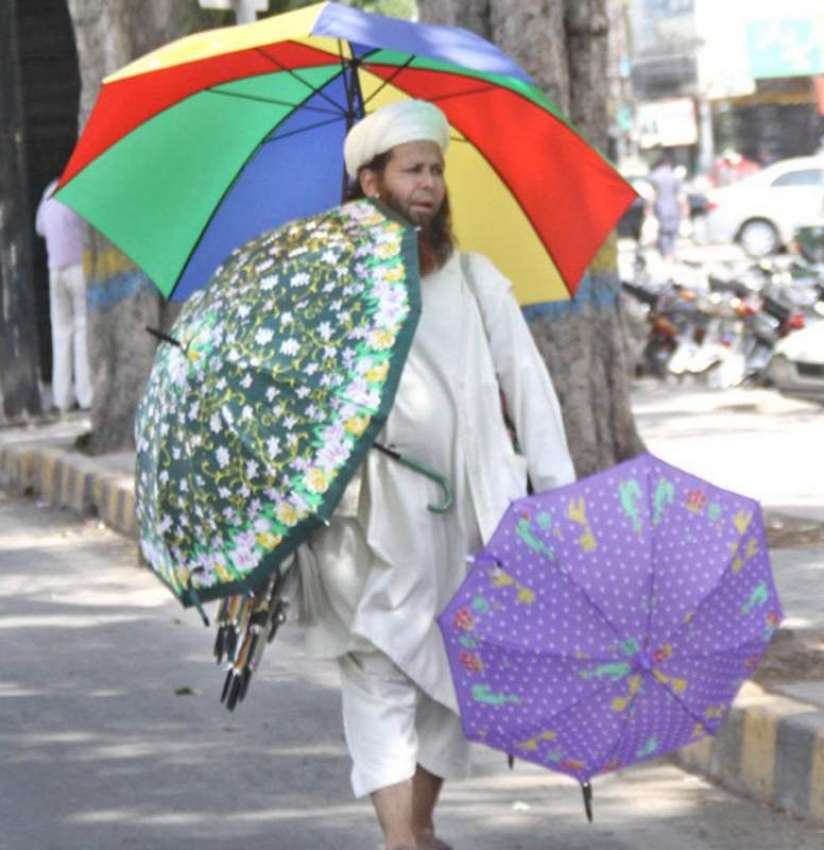 لاہور: ایک محنت کش چھتریاں فروخت کرنے کے لیے گاہکوں کا انتظار ..