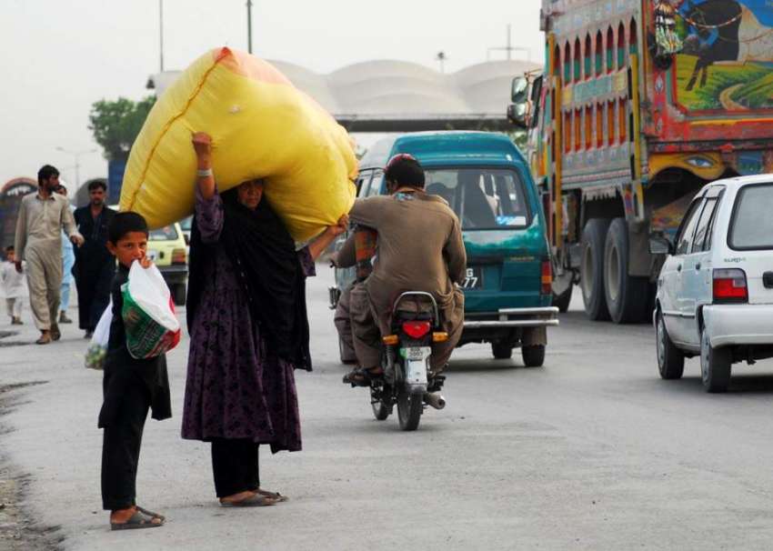 راولپنڈی: ایک خاتون بھاری سامان سر پر اٹھائے روڈ کراس کر ..
