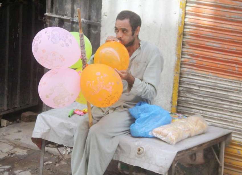 لاہور: ایک محنت کش غبارے فروخت کرنے کے لیے ان میں ہوا بھر ..