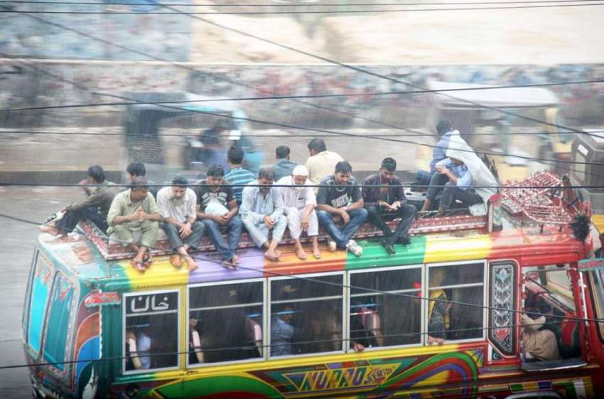 کراچی: مسافر بارش کے دوران بس کی چھت پر بیٹھ کر سفر کر رہے ..