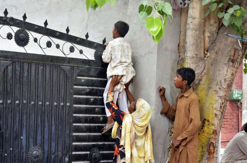 لاہور: ایک عورت نے بچے کو اٹھا رکھا ہے جو دروازے کے اوپر سے ..
