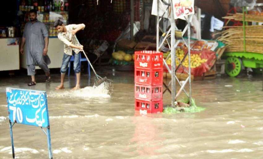 لاہور: ایک دوکاندار بارش کے بعد جمع ہونے والا پانی نکال رہا ..