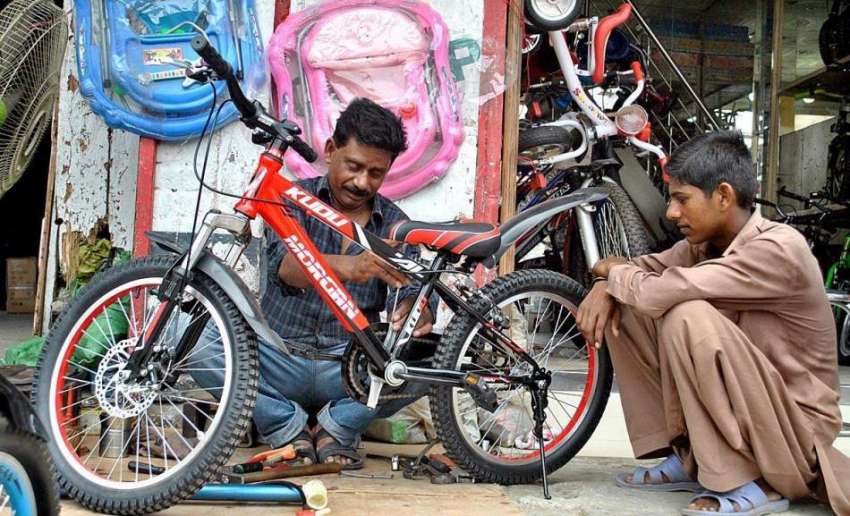 لاہور: ایک محنت کش اپنی دوکان پر بچے کی سائیکل تیار کر رہا ..