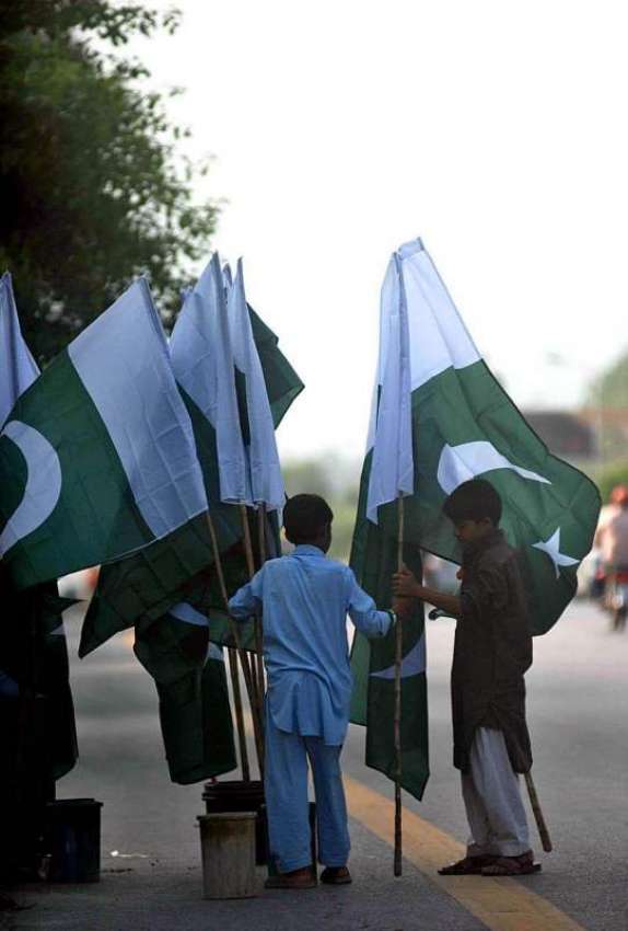 اسلام آباد: ایک بچہ سڑک کنارے پاکستان پارچم فروخت کے لیے ..