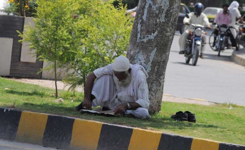 راولپنڈی: ایک معمر شہری روڈ کنارے سبزہ زار پر بیٹھے اخبار ..