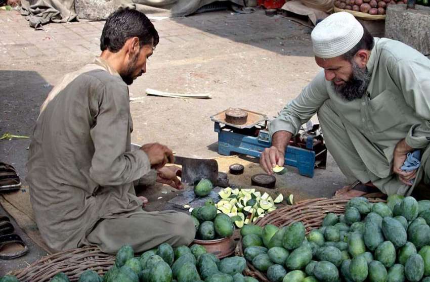 فیصل آباد: روڈ کنارے بیٹھا محنت کش گاہک کے لیے آم کاٹ رہا ..