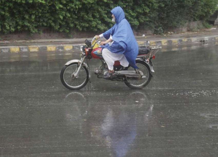 لاہور: موٹر سائیکل سوار شہری بارش سے بچنے کے لیے برساتی پہنے ..