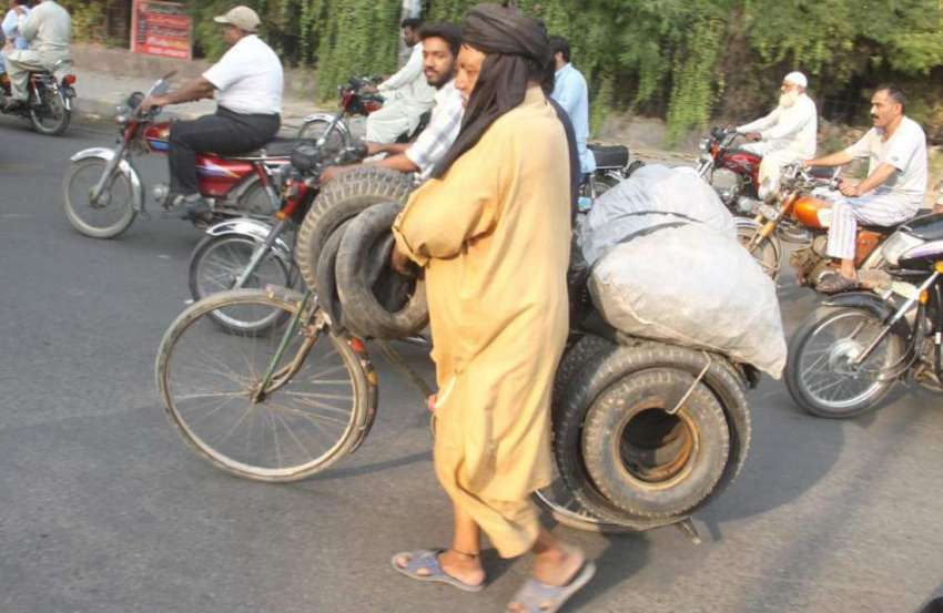 لاہور: ایک محنت کش سائیکل پر پرانے ٹائر رکھے فروخت کے لیے ..