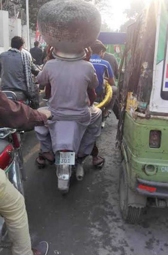 لاہور: ایک موٹر سائیکل سوار شخص سر پر دیگ اٹھائے جا رہا ہے۔
