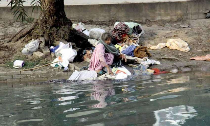 لاہور: ایک خاتون نہر کنارے بیٹھے کپڑے دھو رہی ہے۔