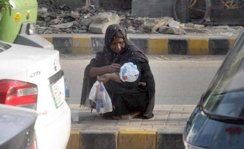 لاہور: ایک بھیکارن خاتون ڈیوائیڈر پر بیٹھی اپنے بچے کو خوراک ..