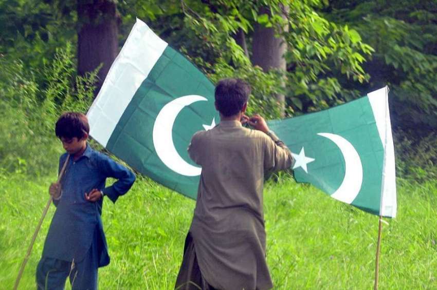 اسلام آباد: دو نوجوان سڑک کنارے قومی پرچم فروخت کے لیے سجائے ..