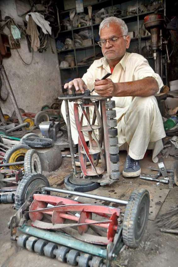 لاہور: ایک بزرگ کاریگر گھاس کاٹنے والی مشین مرمت کرنے میں ..