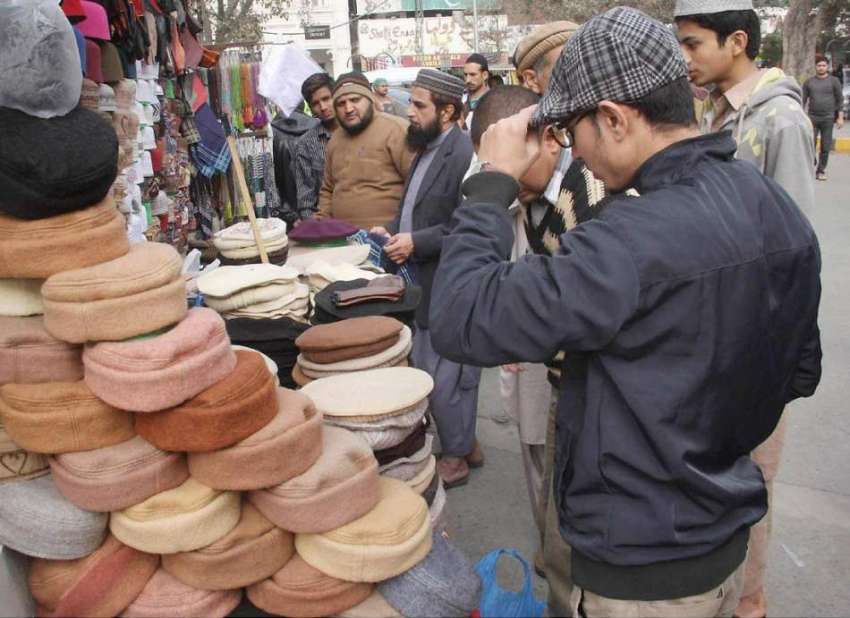 لاہور: شہری سردی کی شدت سے بچنے کے لیے ایک سٹال سے گرم ٹوپیاں ..