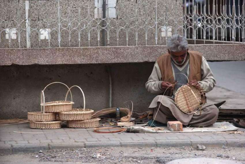 راولپنڈی: ایک مزدور فٹ پاتھ پر بیٹھا روایتی ٹوکریاں بنا ..