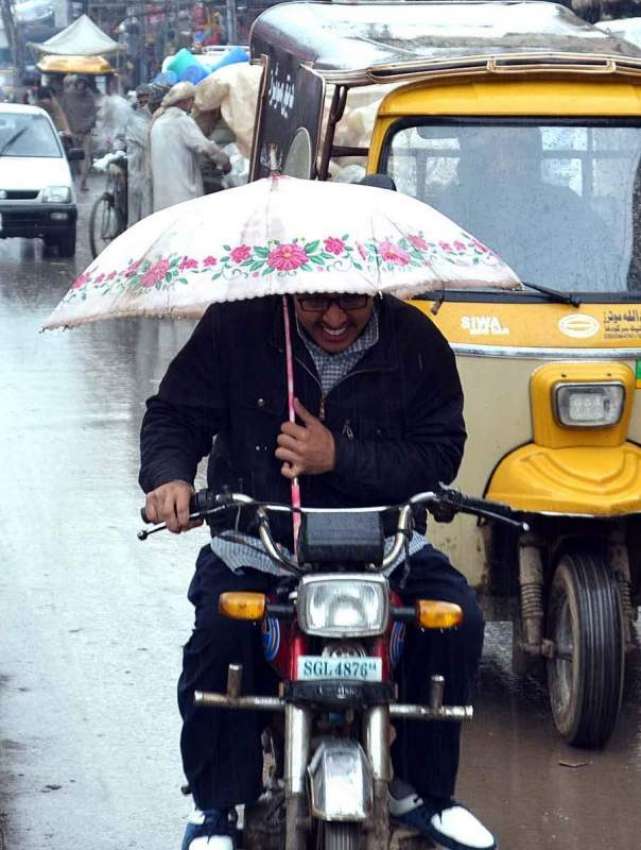 سرگودھا: ایک موٹرسائیکل سوار بارش سے بچنے کے لیے چھتری تانے ..
