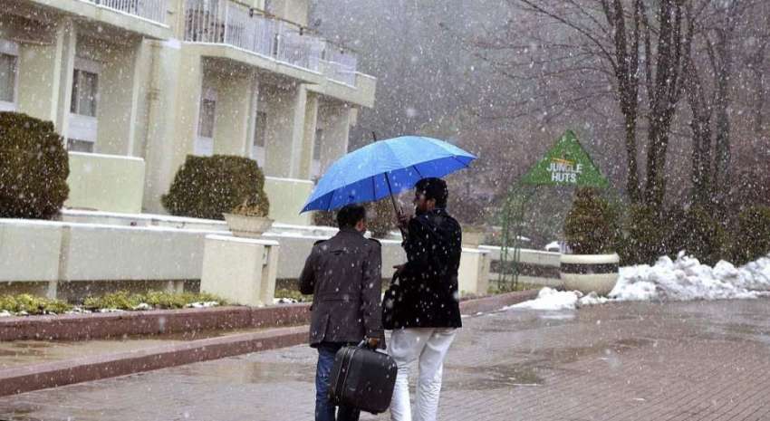 مری: برفباری سے بچنے کے لیے دو شہری چھتری تانے جا رہے ہیں۔