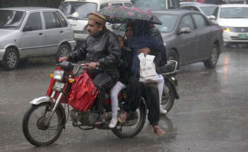 لاہور: شہر میں ہونے والی بارش کے دوران موٹر سائیکل سوار فیملی ..