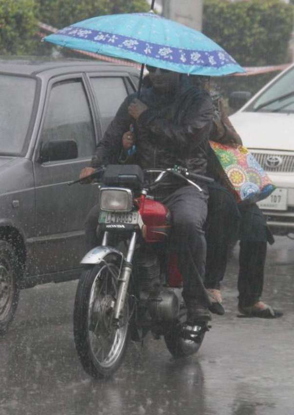لاہور: شہر میں ہونے والی بارش کے دوران موٹر سائیکل سوار فیملی ..